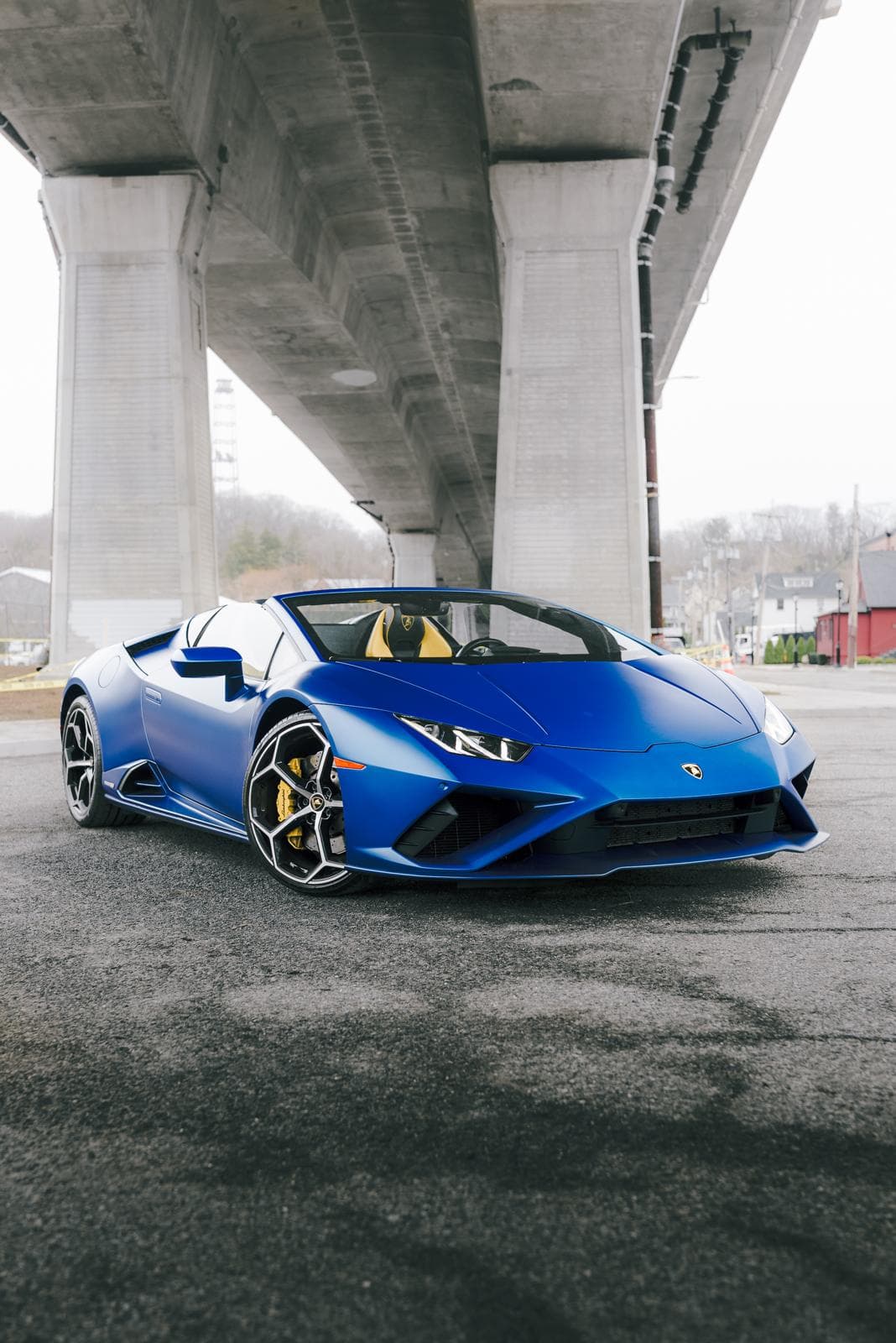 Matte blue Lamborghini Huracán EVO Spyder with the top down, parked beneath a concrete overpass