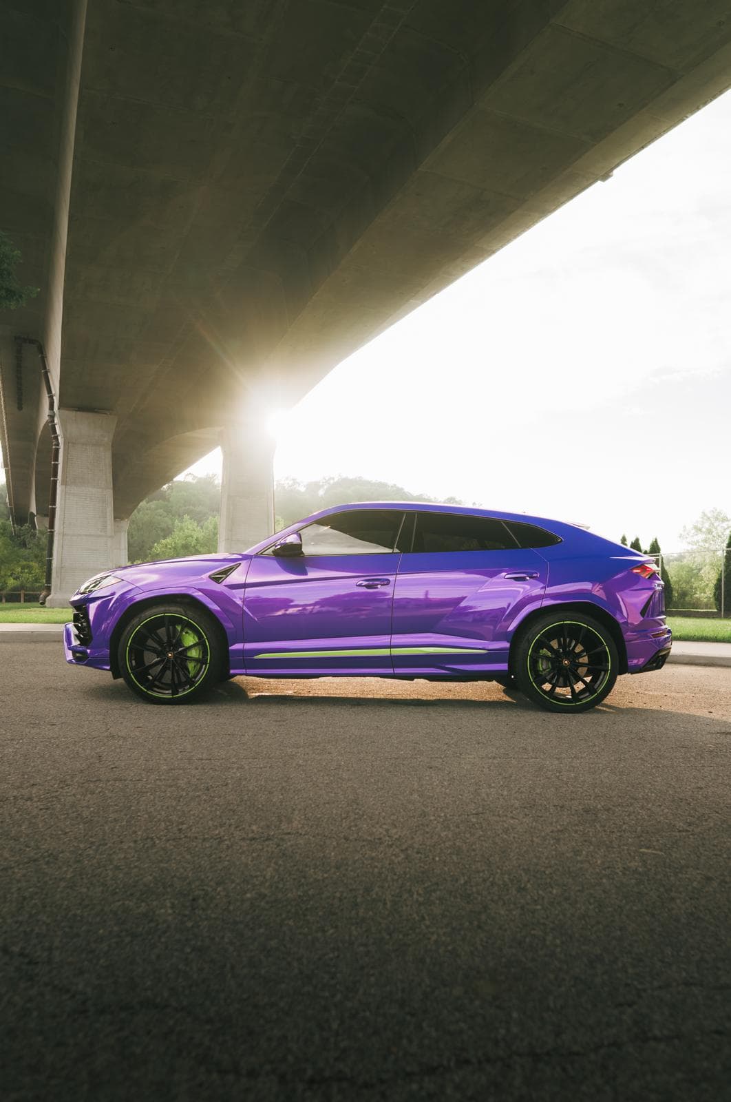 Purple Lamborghini Urus in side profile under a highway overpass, with lime green wheel rims and sill stripe